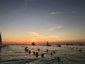 Silhouette people swimming in sea against sky during sunset