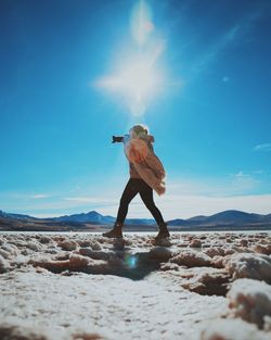 Side view of woman photographing while standing on landscape during sunny day