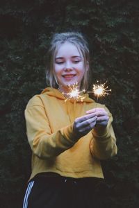 Smiling teenage girl holding illuminated sparklers