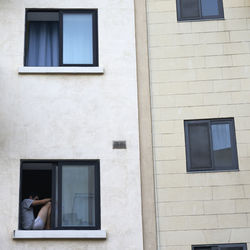 Low angle view of man sitting on building window sill