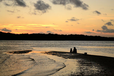 Silhouette people standing on beach against sky during sunset
