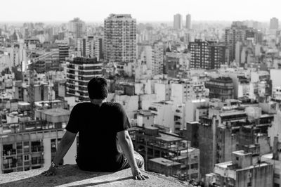 Rear view of man sitting on terrace overlooking cityscape