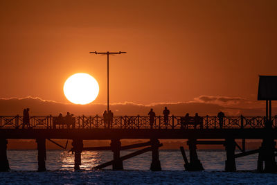 Silhouette pier over sea against orange sky