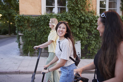 Young female friends spending time together outdoors riding electric scooters