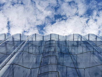 Low angle view of modern building against sky with wavy glass facade