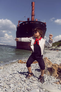 Fashionable boy child with long hair dance next to a large ship that ran aground near novorossiysk