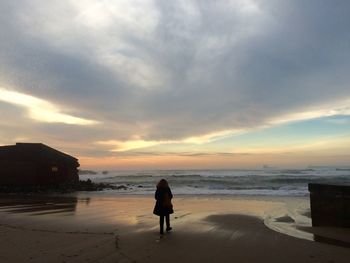 Rear view of woman standing on beach against sky during sunset