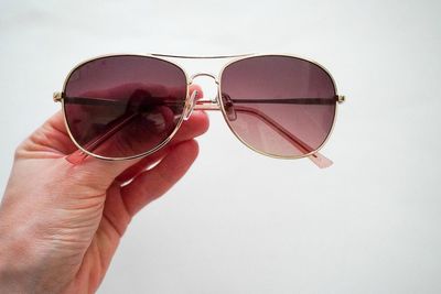 Close-up of hand holding sunglasses against white background