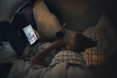 High angle view of boy using digital tablet lying on bed at home