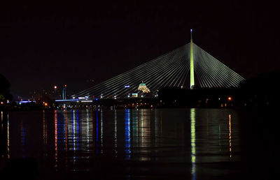 Illuminated city by river against sky at night