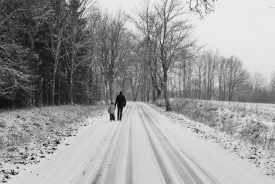 Rear view of man walking on snow covered road