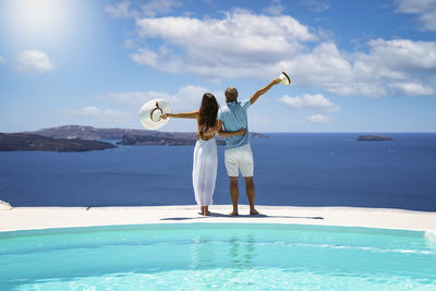 Rear view of couple with arms outstretched standing against sea and sky
