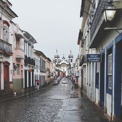 Wet street amidst buildings against sky during rainy season