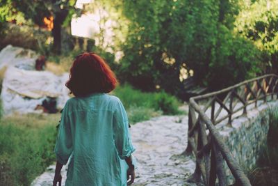 Rear view of woman standing on footpath against trees