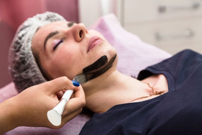 Applying cream mask for carbon peeling on the face of an adult woman.