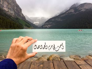 Cropped hand holding text against lake and mountains