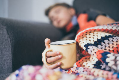 Boy holding cup while sleeping on sofa at home