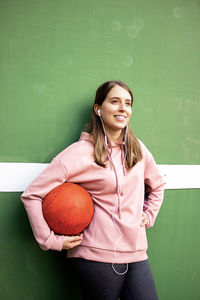 Young woman holding basketball against wall