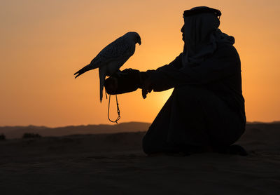 Silhouette woman with arms outstretched standing at beach against sky during sunset