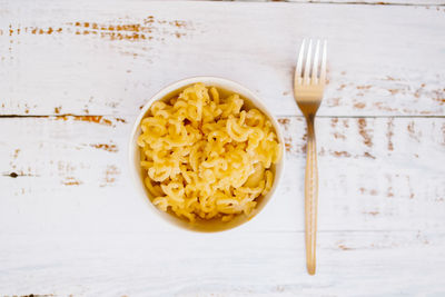 Classic homemade macaroni and cheddar cheese on black plate with a fork on white wooden table.
