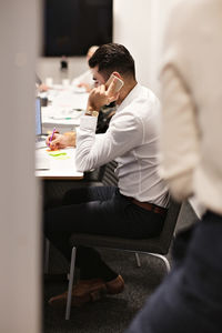 Businessman talking on smart phone while writing in adhesive note at board room