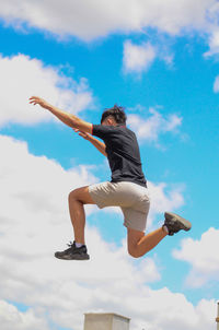 Low angle view of man jumping against cloudy sky