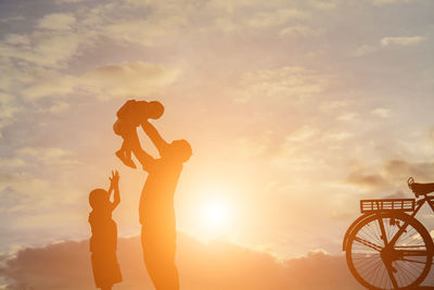 Silhouette people with arms raised against sky during sunset