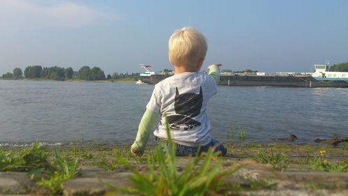 Rear view of boy pointing at lake against sky