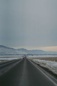 Road amidst snow covered landscape against sky