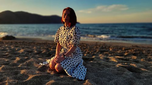 Rear view of woman standing at beach against sky during sunset