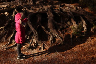 Side view of girl touching tree roots while standing in forest