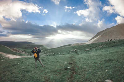 Rear view of man standing on land against cloudy sky