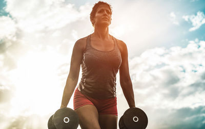 Low angle view of woman exercising with dumbbell against sky