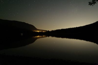 Silhouette of lake and mountain against star field at night