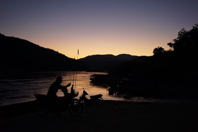 Silhouette people by lake against clear sky during sunset