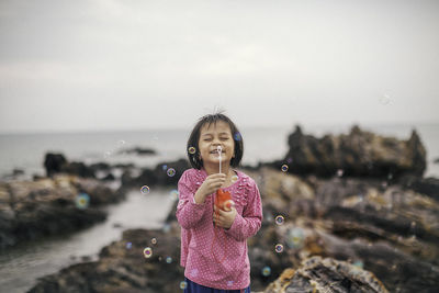 Portrait of girl holding bubble wand  against sky