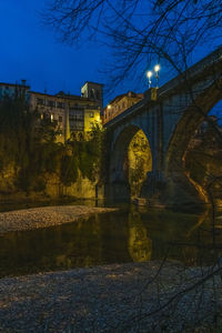 Arch bridge over river by buildings against sky at night