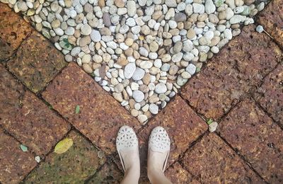 Low section of woman standing by pebbles on footpath