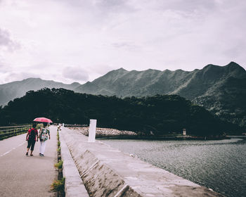 Rear view of family walking on bridge against cloudy sky