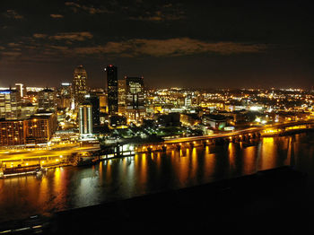 Illuminated buildings by river against sky in city at night