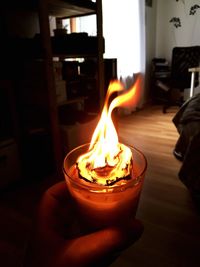 Close-up of hand holding lit candle at home