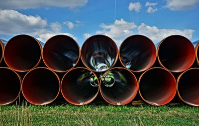 Stack of pipes on field against sky