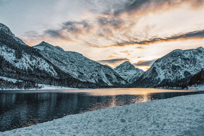 Scenic view of lake by snowcapped mountains against sky during sunset