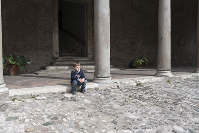 Boy sitting by column of old building
