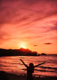 Silhouette person standing on beach against orange sky