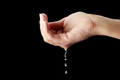 Close-up of hand holding water drop against black background
