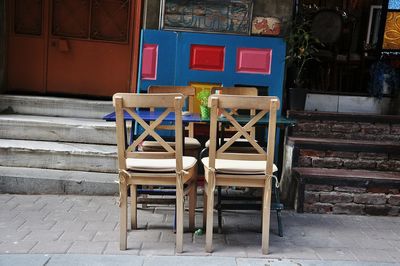 Empty chairs and tables on sidewalk against wall