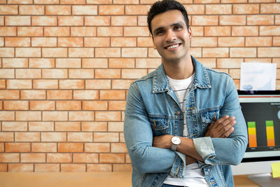 Portrait of a smiling young man standing against brick wall