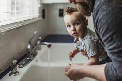 Side view of young boy having hands washed in sink by dad