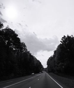 Empty road along trees and against sky